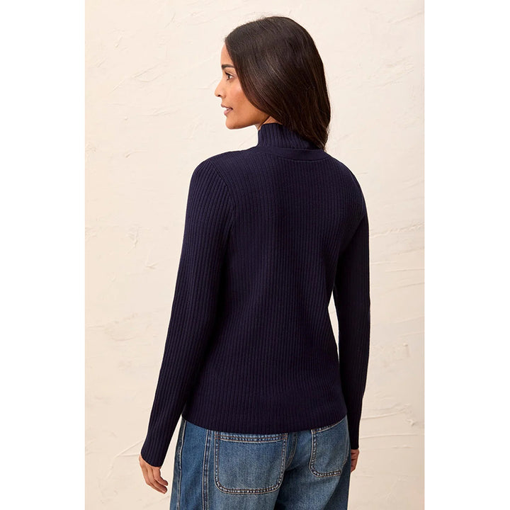 A woman shown from the back wearing a dark navy ribbed cardigan and blue jeans, standing against a light textured wall.
