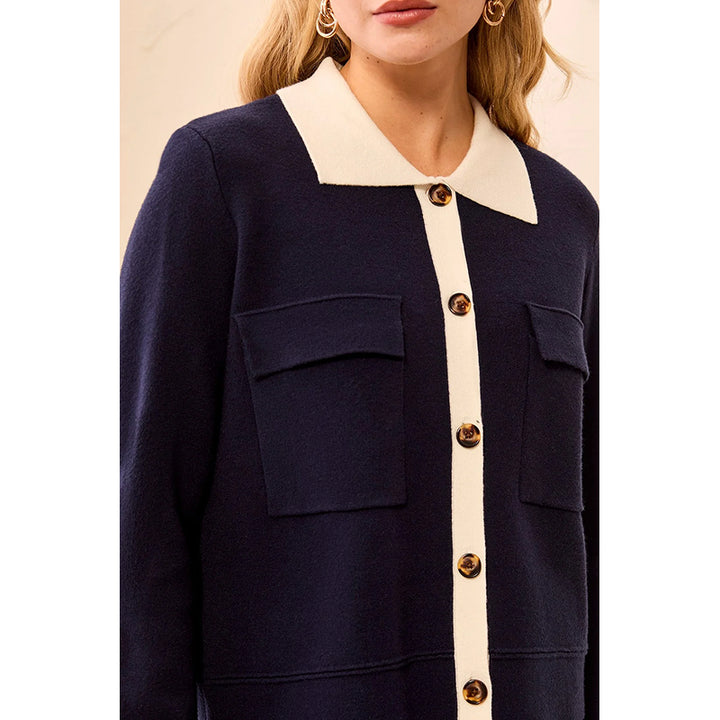 A close-up of a model wearing a navy blue cardigan with a cream-colored collar and center placket, accented by brown buttons.