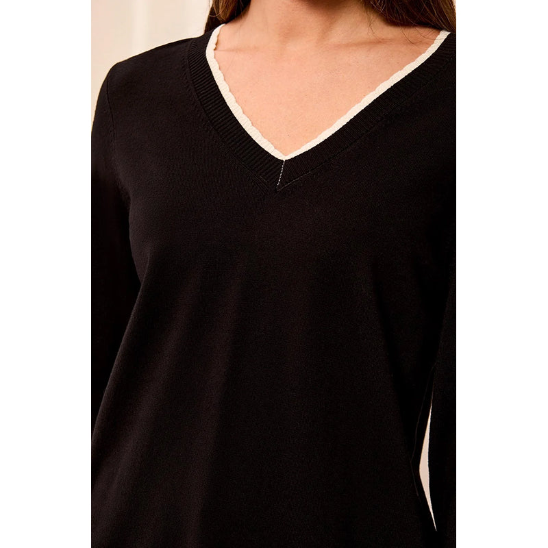 A close-up of a person wearing a black long-sleeve V-neck sweater with a contrasting cream-colored trim along the neckline.