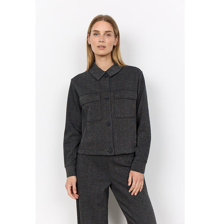 A woman modeling a dark gray textured jacket and matching trousers against a plain white studio background.