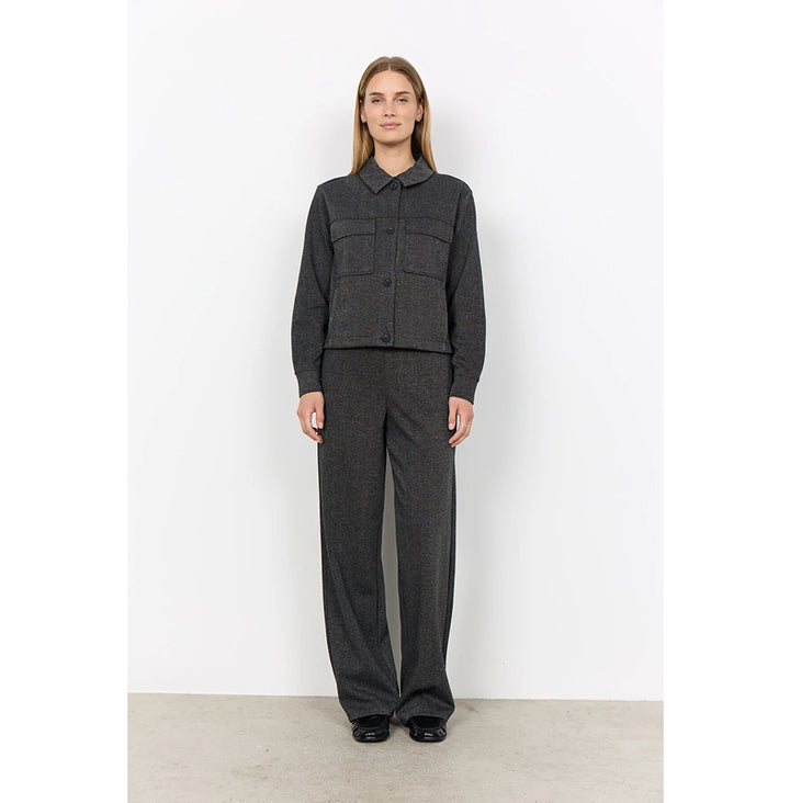 A model stands against a white studio wall wearing a dark gray textured two-piece set consisting of a cropped long-sleeve button-front jacket with a collar and matching wide-leg trousers.