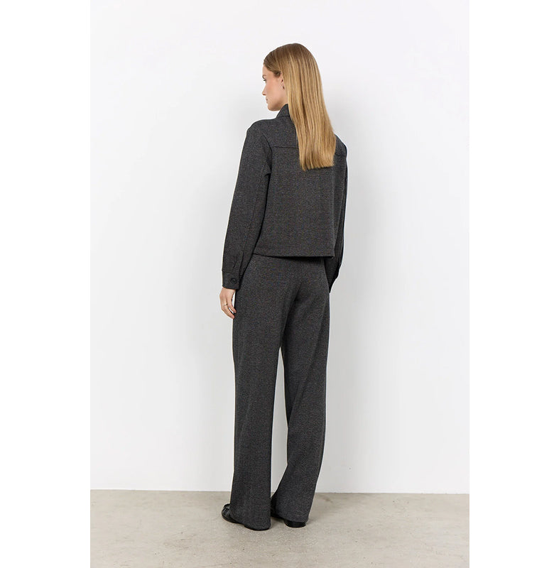 A woman stands with her back to the camera wearing a dark charcoal gray knit matching set consisting of a cropped long-sleeve top and wide-leg trousers, set against a plain white studio wall.