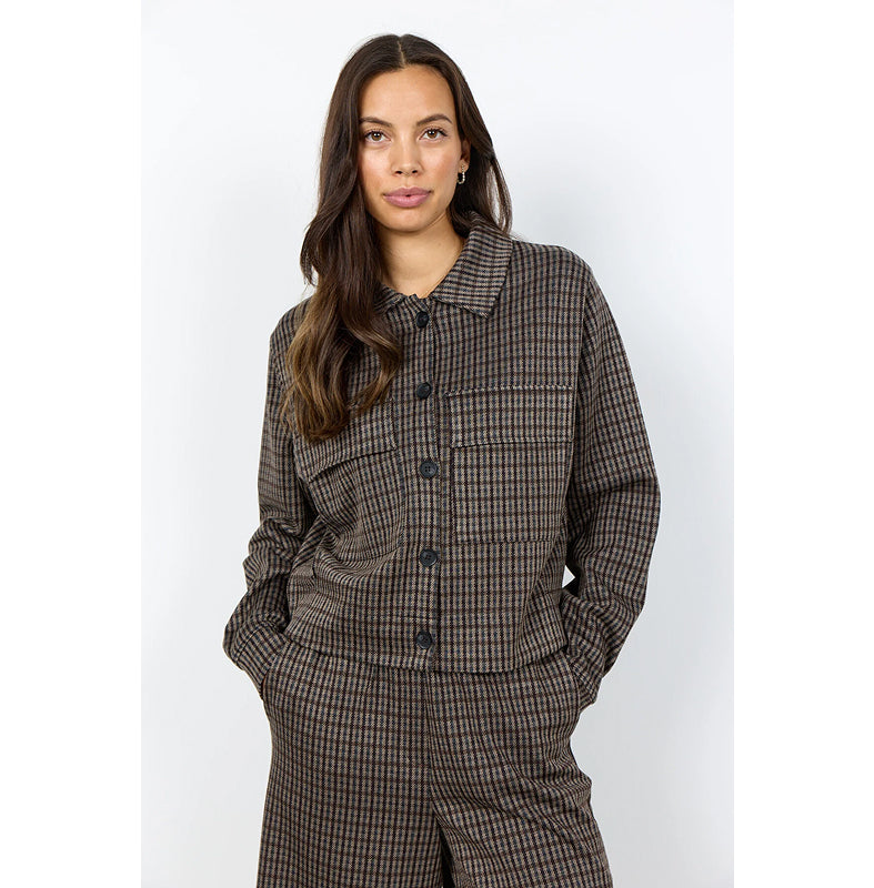 A woman modeling a brown and black checkered button-up shirt and matching trousers against a light gray studio background.