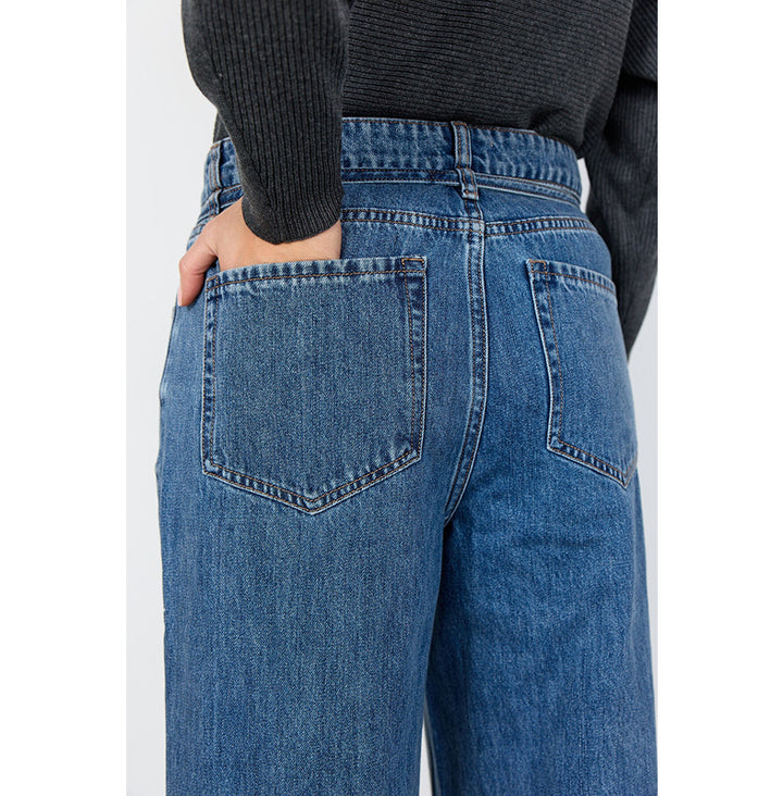 Close-up back view of a person wearing blue denim jeans with a dark ribbed sweater, showing the back pockets and waistband.