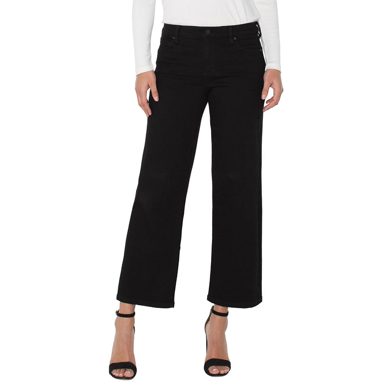 Black wide-leg cropped jeans shown on a model from the waist down, paired with a white long-sleeve top and black high-heeled sandals against a plain white background.