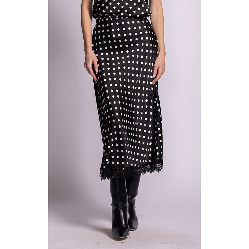 A black midi skirt with white polka dots and a lace hem, worn by a model with black knee-high boots against a light gray studio background.