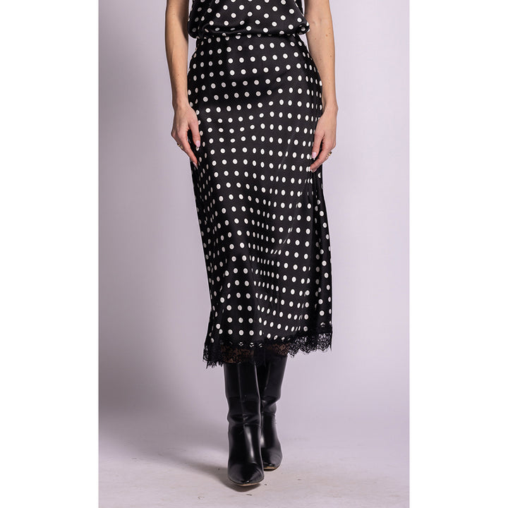 A black midi skirt with white polka dots and a lace hem, worn by a model with black knee-high boots against a light gray studio background.