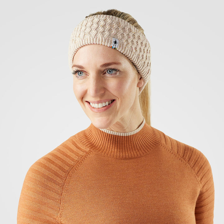 Woman wearing a beige knitted headband and orange sweater on a white background