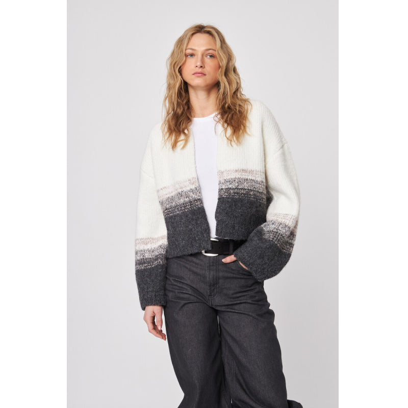 Woman wearing a white and gray patterned cardigan with a plain background