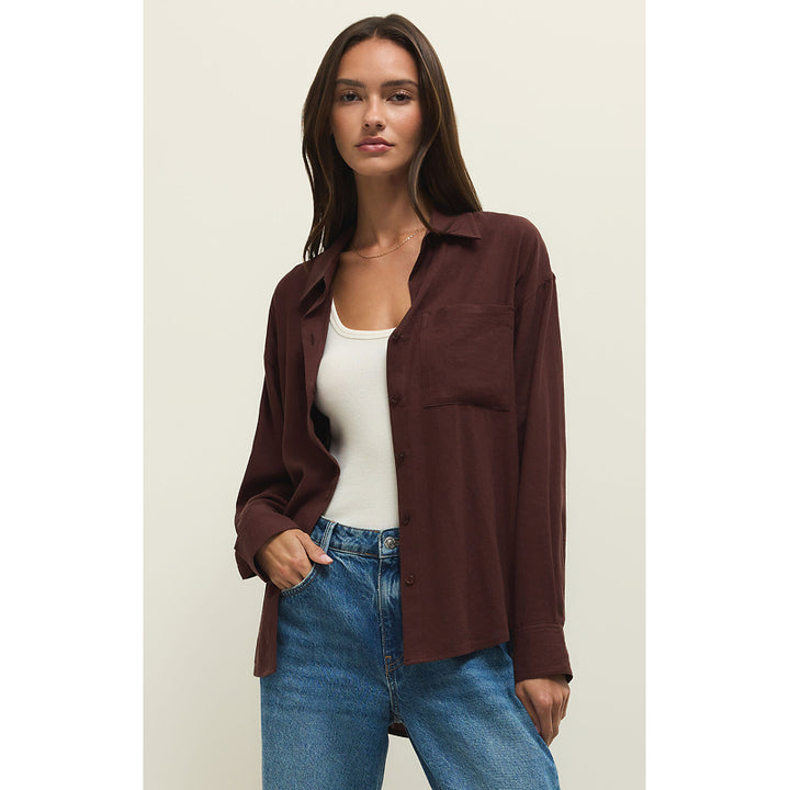 Woman wearing a brown shirt over a white top and blue jeans on a beige background