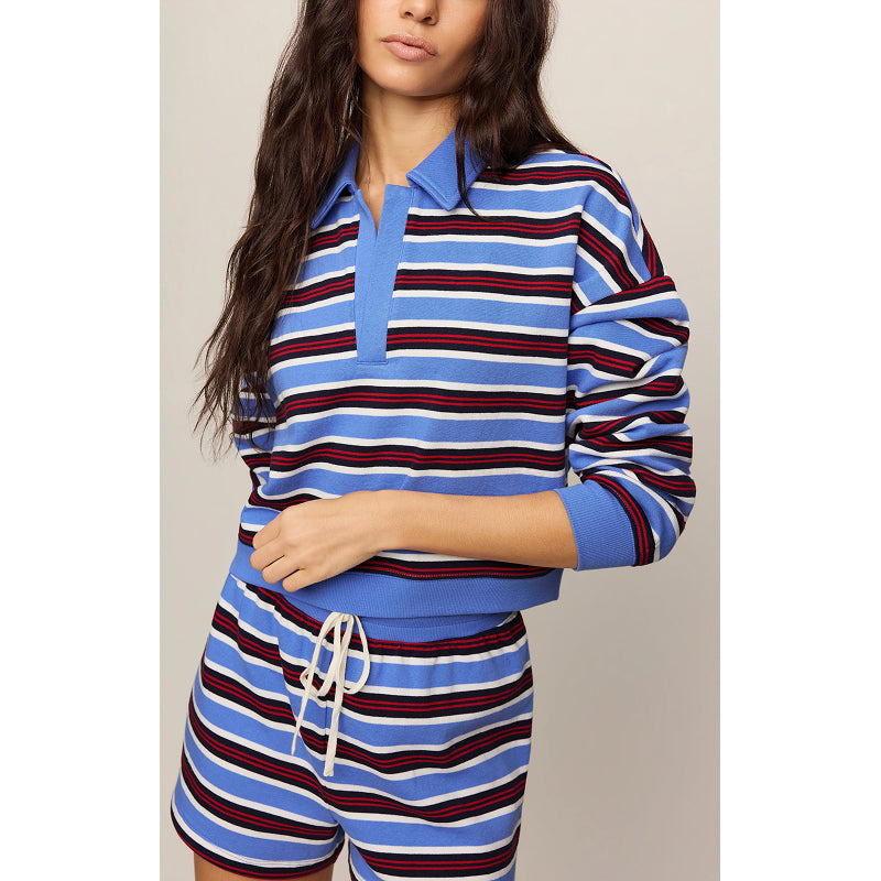 A woman wearing a matching blue, white, and red striped lounge set consisting of a long-sleeve polo shirt and shorts with a white drawstring.