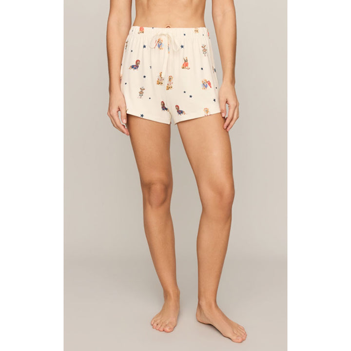 A model wearing cream-colored shorts with a whimsical, colorful cartoon animal print, standing against a neutral beige studio background.