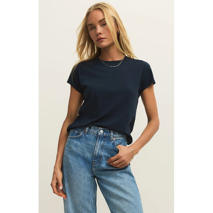 Woman wearing a navy t-shirt and blue jeans against a plain background