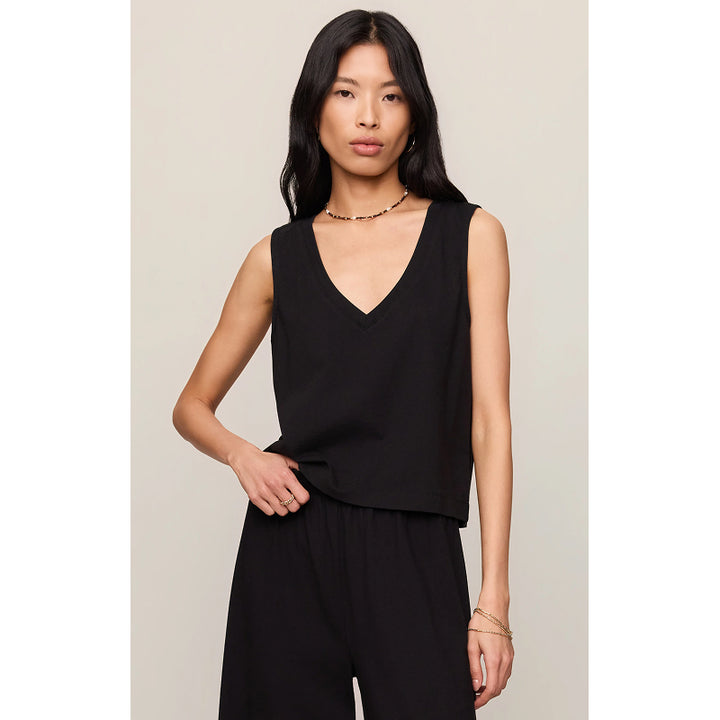 A woman modeling a black sleeveless V-neck top with a relaxed fit, paired with black pants, against a light beige studio background.