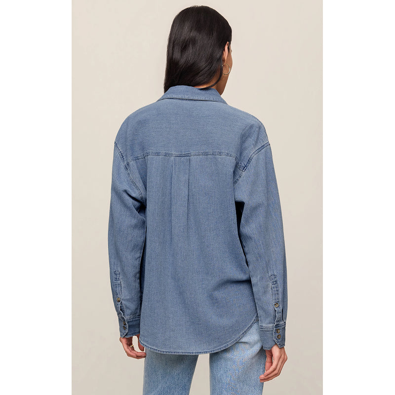 A model shown from the back wearing an oversized blue denim button-up shirt and light-wash jeans against a plain beige studio background.