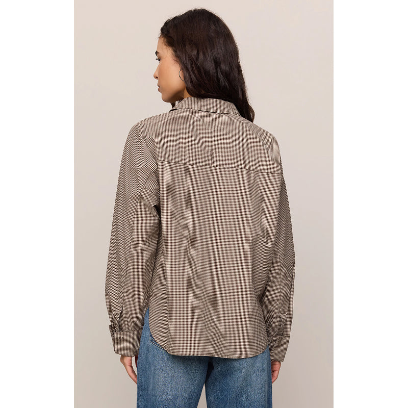 A woman shown from the back wearing a brown and beige checkered button-down shirt with blue jeans, set against a plain light beige studio background.