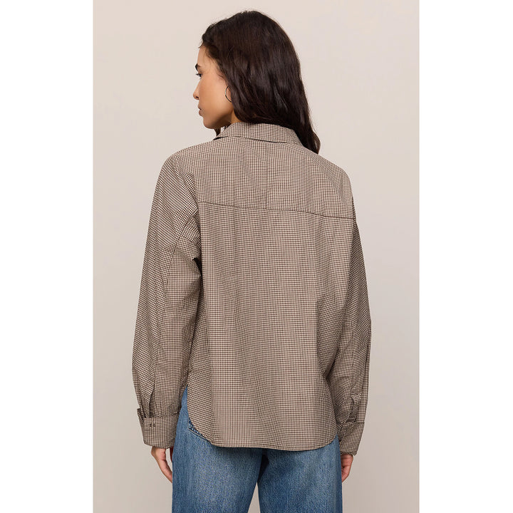 A woman shown from the back wearing a brown and beige checkered button-down shirt with blue jeans, set against a plain light beige studio background.