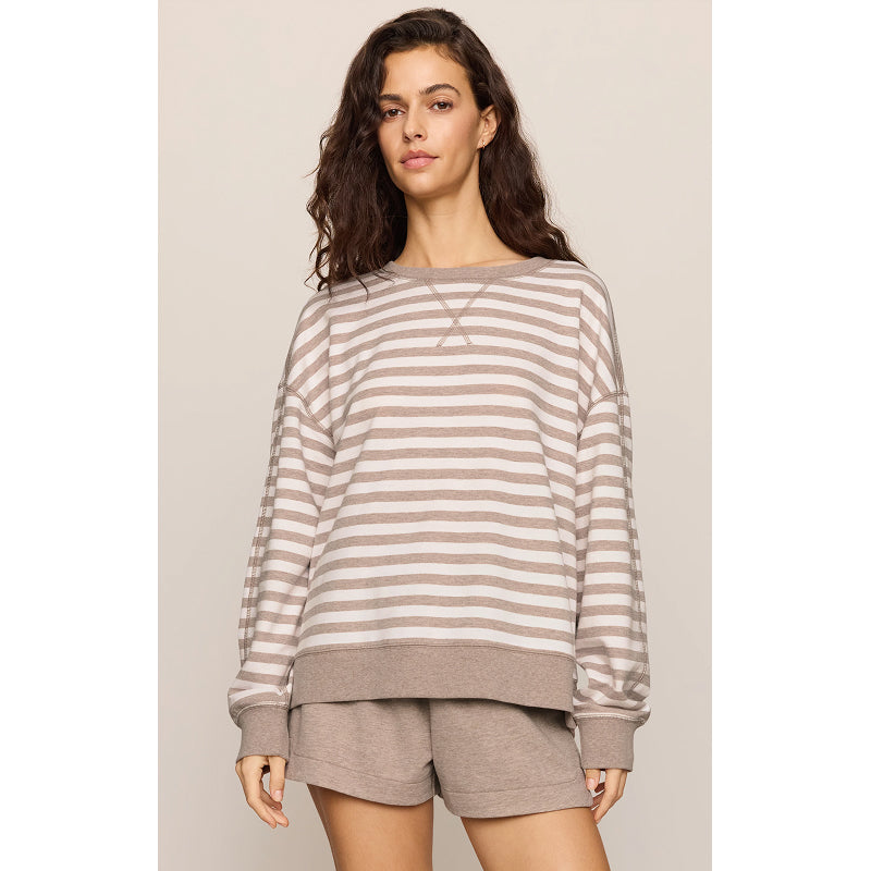 A woman modeling a long-sleeve crewneck sweatshirt with horizontal taupe and off-white stripes, paired with matching taupe shorts, against a solid light beige background.