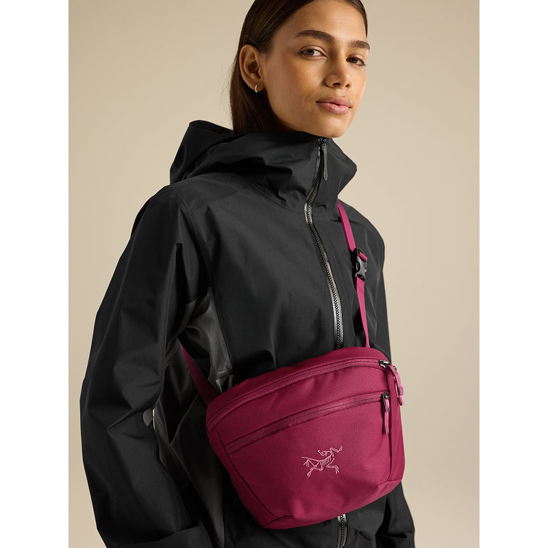 A woman wearing a black hooded jacket and a magenta Arc'teryx crossbody bag, shown from the chest up against a plain beige background.