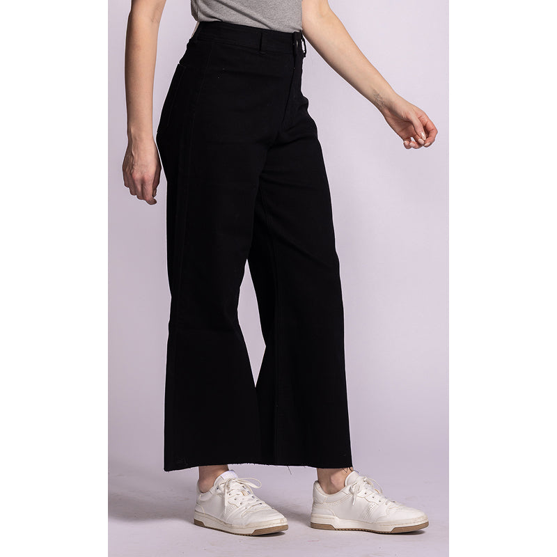 A model wearing black wide-leg cropped pants, a gray top, and white sneakers, shown from the waist down against a light lavender studio background.