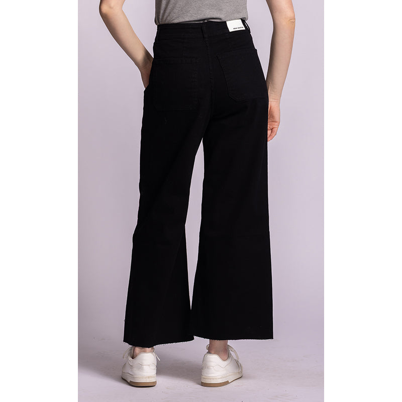 A model from the back wearing black wide-leg cropped pants, a gray t-shirt, and white sneakers against a light lavender studio background.