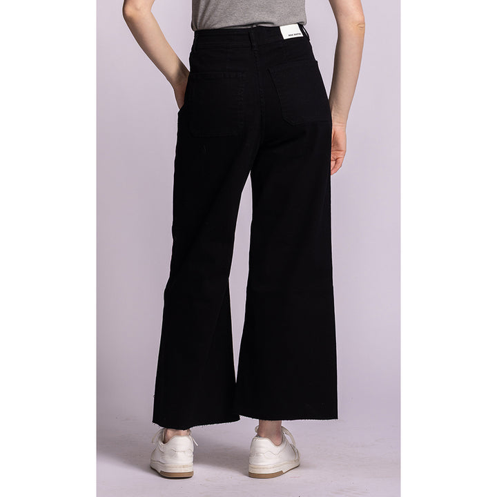 A model from the back wearing black wide-leg cropped pants, a gray t-shirt, and white sneakers against a light lavender studio background.
