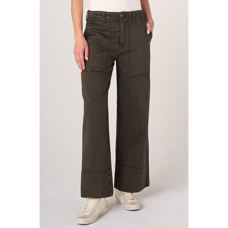 A person wearing dark olive green wide-leg cropped pants with a white top and off-white sneakers, standing against a light gray studio background.