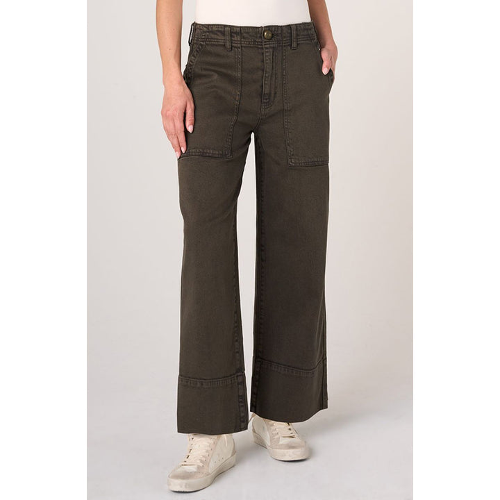A person wearing dark olive green wide-leg cropped pants with a white top and off-white sneakers, standing against a light gray studio background.