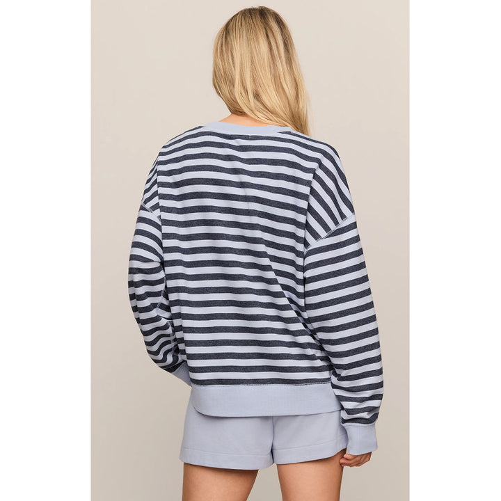 A woman shown from the back wearing a navy and gray striped long-sleeve sweatshirt and light gray shorts against a plain beige studio background.