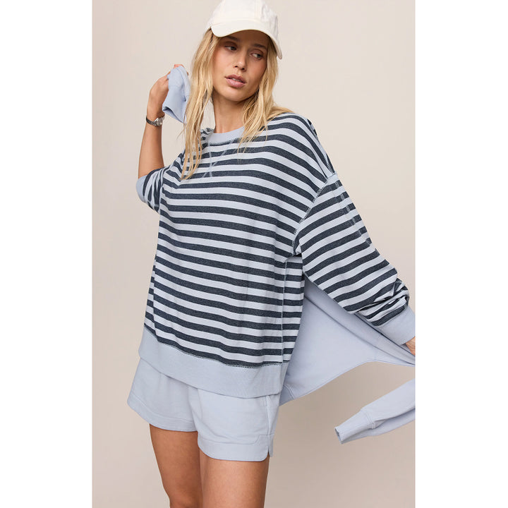 A woman modeling an oversized navy and white striped long-sleeve top with light blue shorts and a white cap, set against a plain beige studio background.