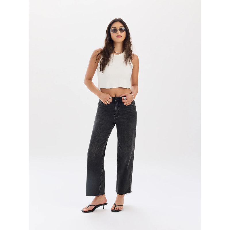 A woman modeling a pair of wide-leg black denim jeans, styled with a white ribbed crop top, black sandals, and sunglasses, against a plain white studio background.