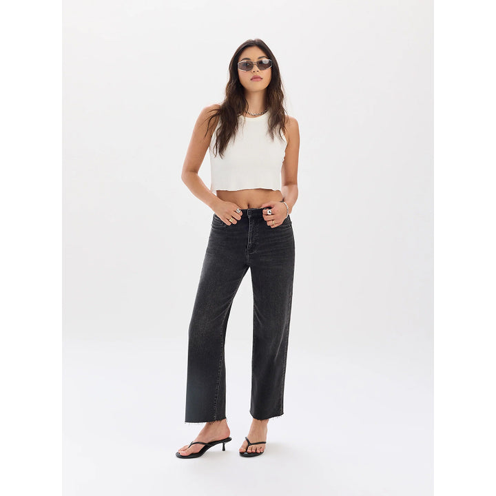 A woman modeling a pair of wide-leg black denim jeans, styled with a white ribbed crop top, black sandals, and sunglasses, against a plain white studio background.