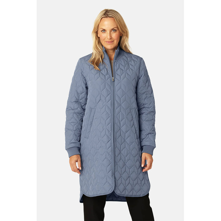 Woman wearing a long quilted blue jacket on a white background