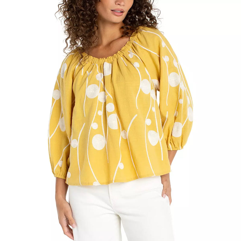 Woman wearing a yellow blouse with white floral patterns on a white background