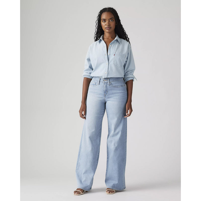 Woman wearing a light blue shirt and jeans on a plain background