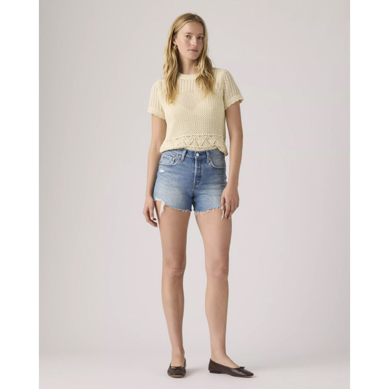 Woman wearing a light yellow top and denim shorts on a plain background