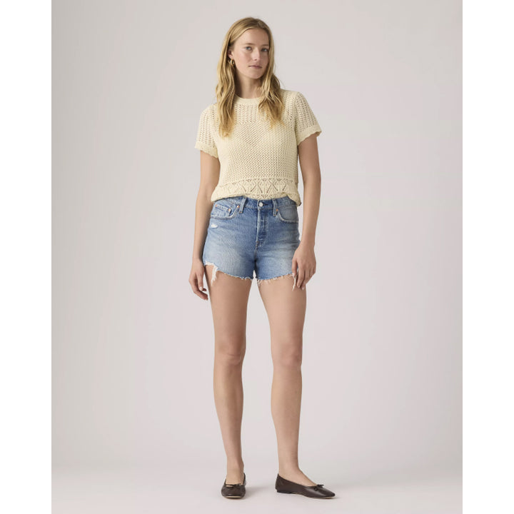 Woman wearing a light yellow top and denim shorts on a plain background