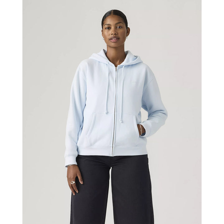 Woman wearing a light blue hoodie and black pants on a plain background