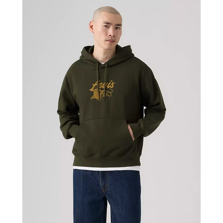 A man wearing an olive green hoodie with a gold 'Levi's' graphic on the chest, paired with blue jeans, standing against a light gray studio background.