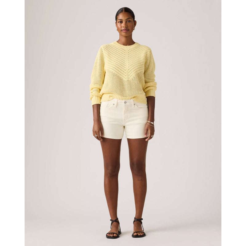 Woman wearing a yellow knitted sweater and white shorts on a plain background