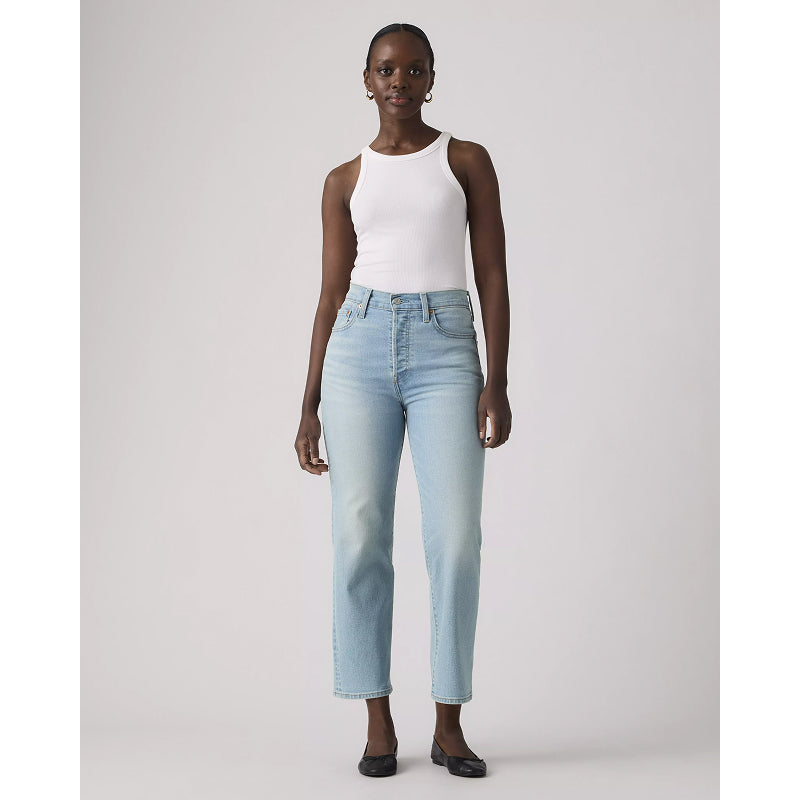 Woman wearing light blue jeans and a white top on a plain background