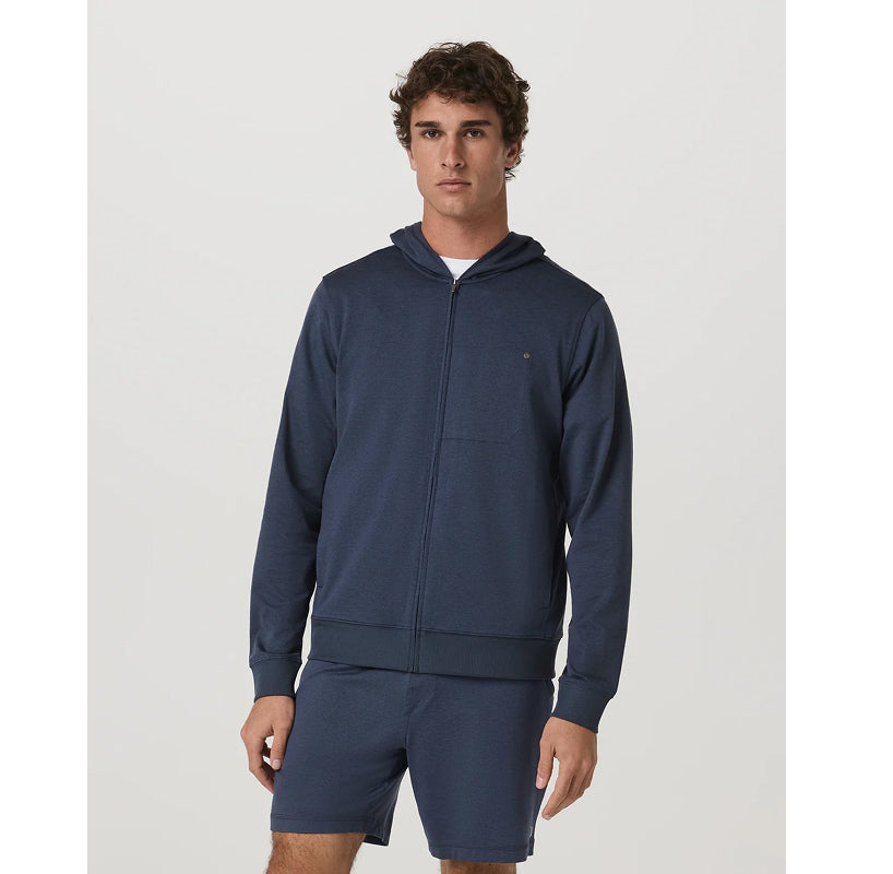 A man modeling a navy blue zip-up hoodie and matching shorts set against a plain light gray studio background.