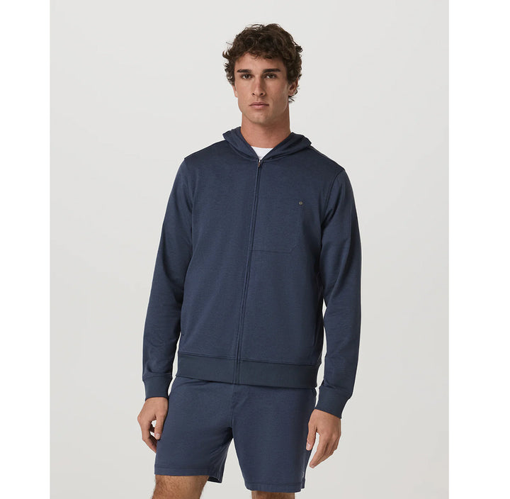 A man modeling a navy blue zip-up hoodie and matching shorts set against a plain light gray studio background.