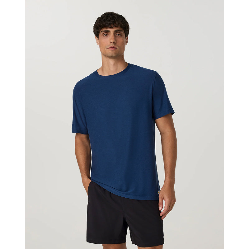 A man wearing a solid navy blue short-sleeve crewneck t-shirt and black athletic shorts, standing against a light gray studio background.