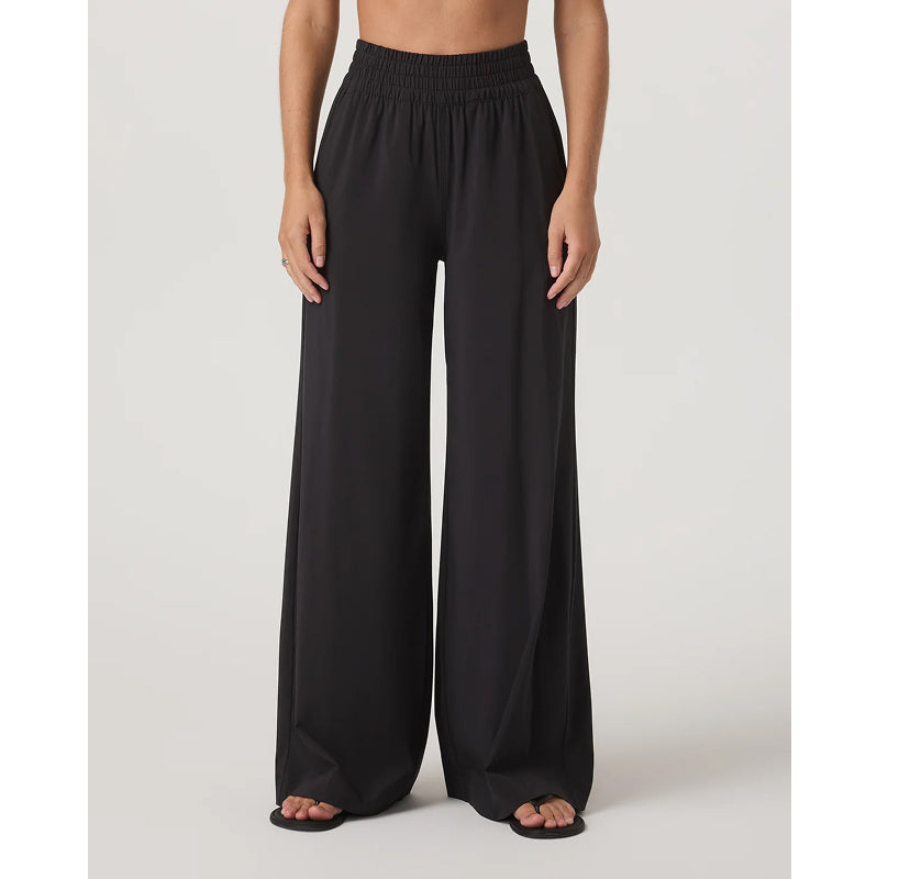 A model wearing black wide-leg pants with an elastic waistband, shown from the waist down against a light gray studio background.
