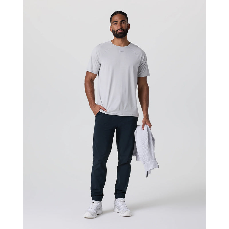 Man wearing a gray t-shirt, dark pants, and white sneakers holding a white towel on a plain background