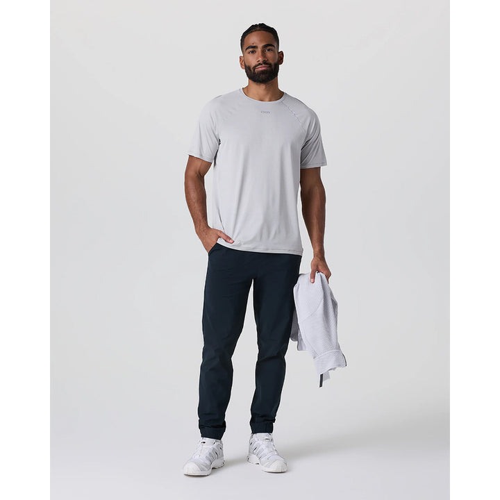 Man wearing a gray t-shirt, dark pants, and white sneakers holding a white towel on a plain background