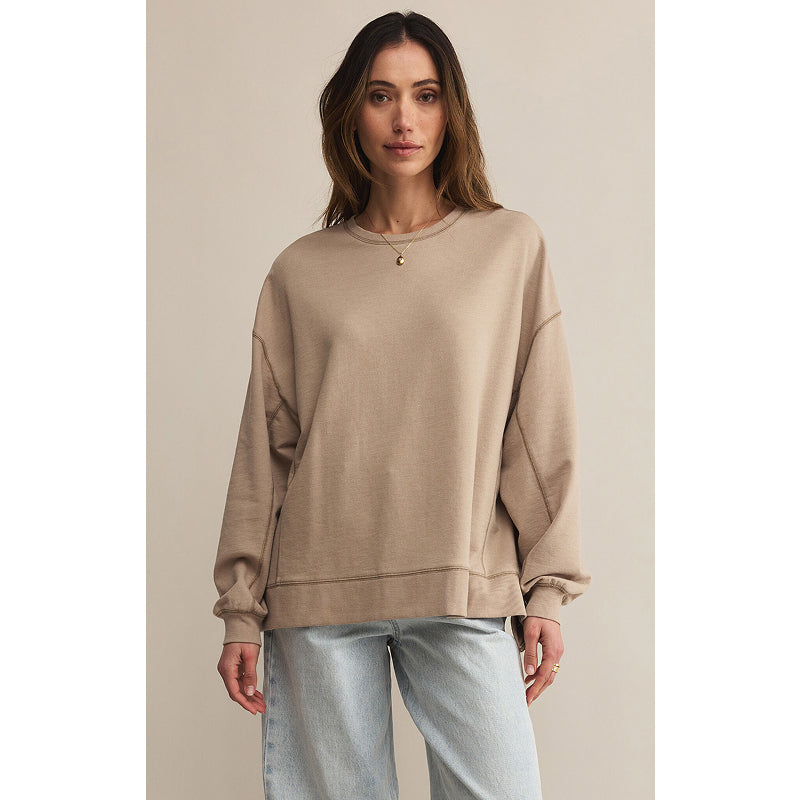 Woman wearing a beige sweatshirt and light blue jeans against a plain background