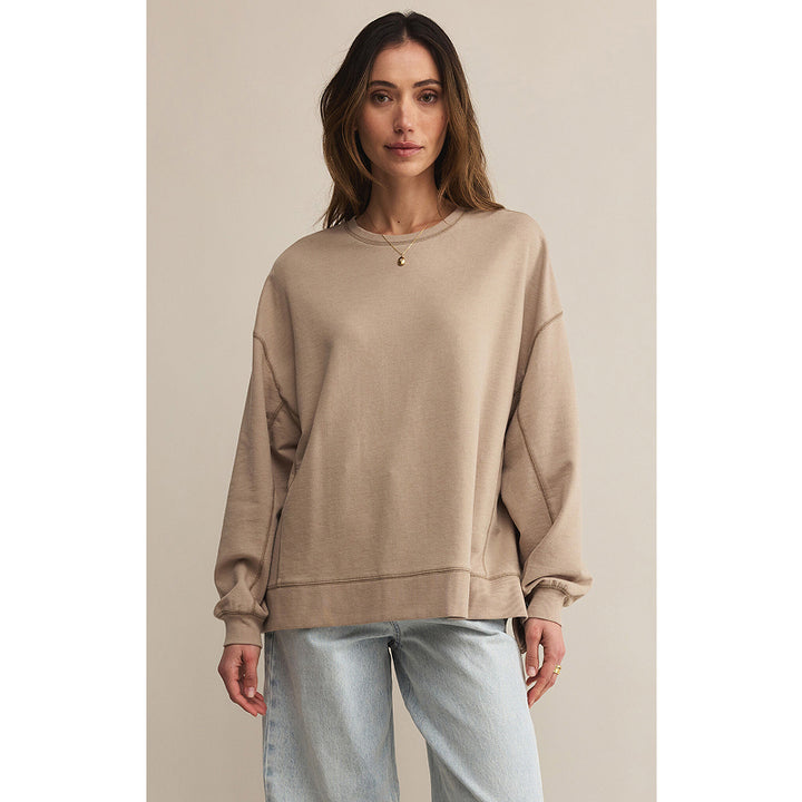 Woman wearing a beige sweatshirt and light blue jeans against a plain background