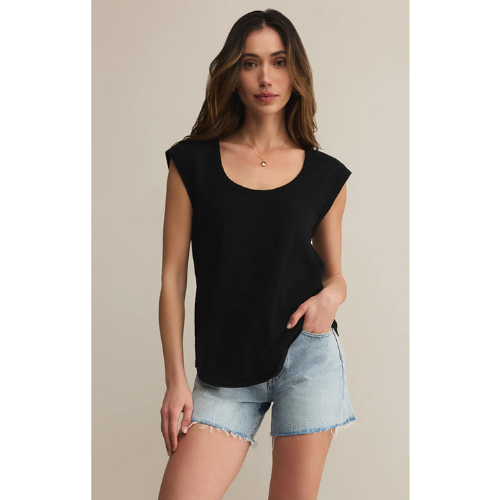 Woman wearing a black sleeveless top and denim shorts on a beige background